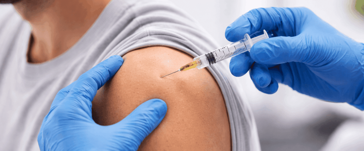 Zorgverlener met blauwe handschoenen geeft een cortisone-injectie in de schouder van een patiënt in een lichte klinische omgeving, close-up gefotografeerd.