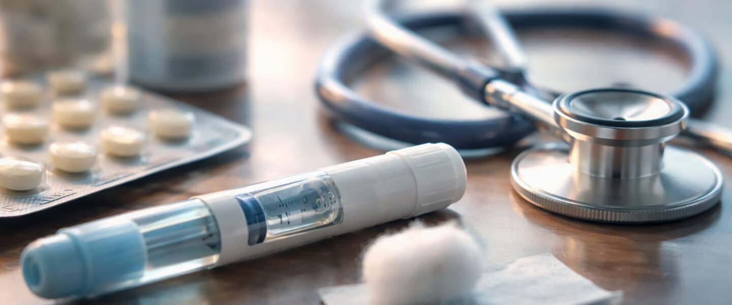 Voorgevulde injectiepen voor cholesterolverlaging op tafel met stethoscoop en medicatie op de achtergrond