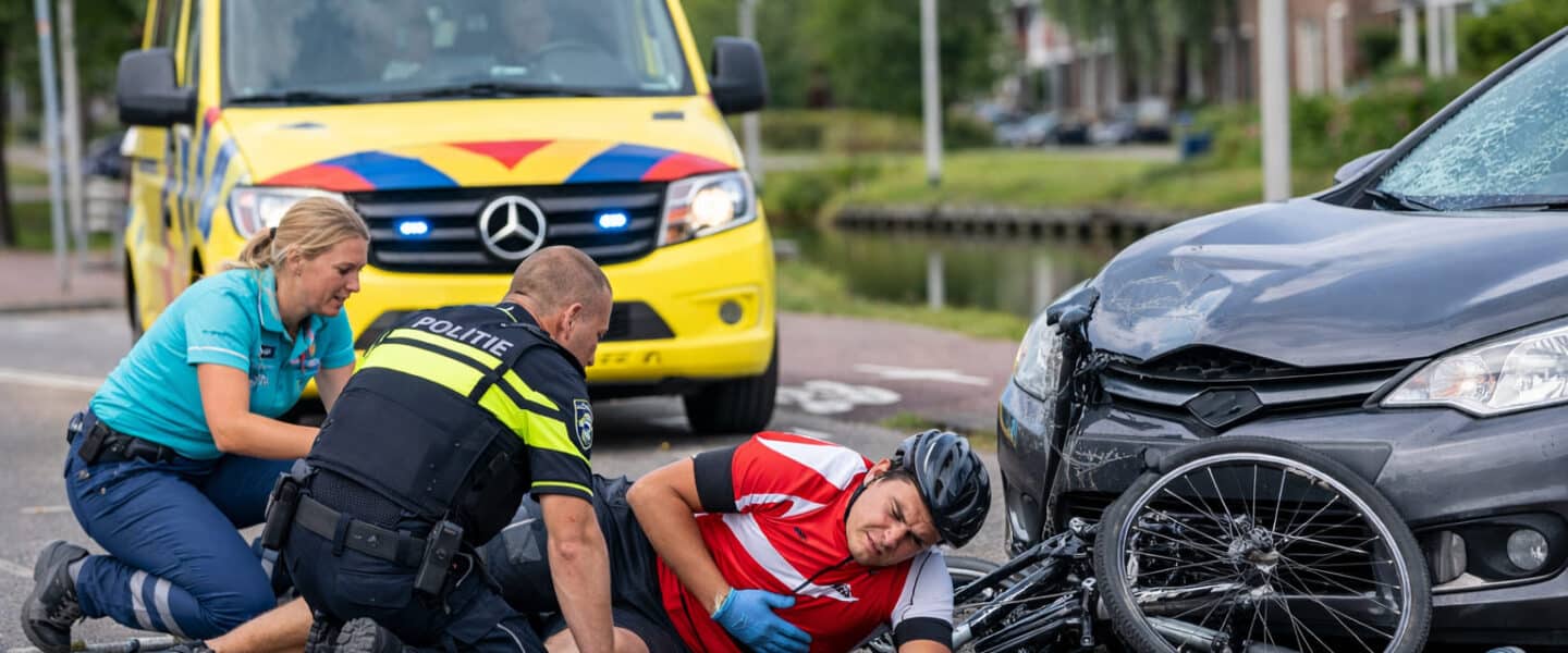 Fietser ligt op de weg na een verkeersongeval in een Nederlandse woonwijk, geholpen door ambulancepersoneel en politie; voorbeeld van buiktrauma dat een miltruptuur kan veroorzaken.