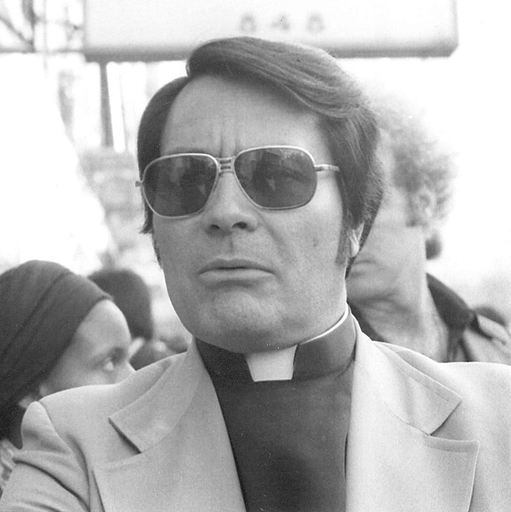 De afgebeelde persoon is Jim Jones, de Amerikaanse sekteleider van de Peoples Temple. De foto is genomen tijdens een anti-uitzettingsrally op zondag 16 januari 1977, voor het International Hotel in San Francisco.