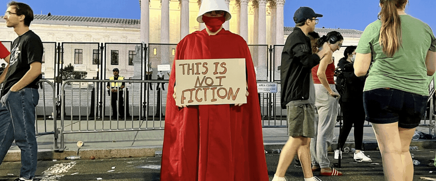 Demonstrant in rood handmaid-kostuum met wit hoofddeksel houdt een bord vast met de tekst “This is not fiction” voor het Amerikaanse Hooggerechtshof