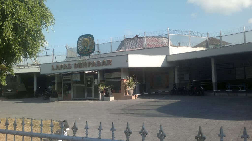 Buitenzijde van de Lapas Denpasar (Kerobokan-gevangenis) op Bali, met laag gebouw, toegangspoort, prikkeldraad op het dak en het officiële opschrift “LAPAS DENPASAR”, gefotografeerd overdag.