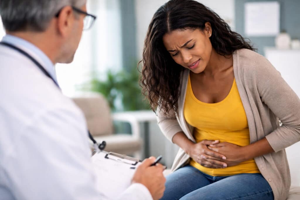 Vrouw met donkere huidskleur die bij de huisarts haar buik vasthoudt vanwege buikpijn
