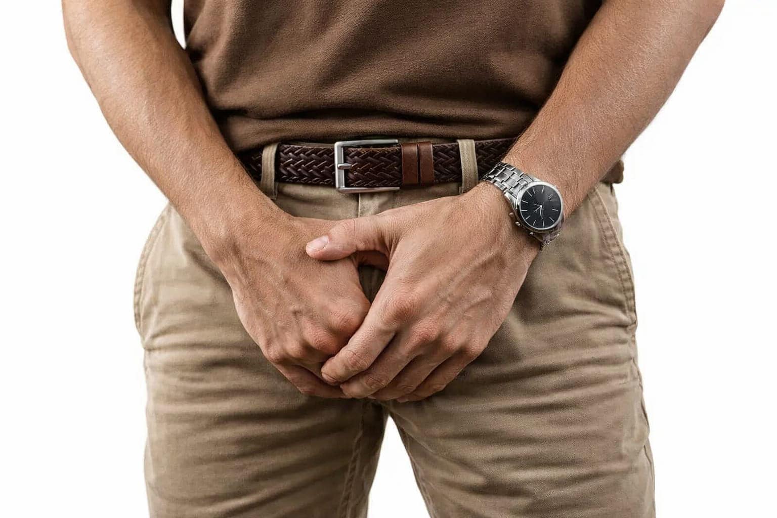 Man in bruine shirt en beige broek die met beide handen zijn geslachtsdelen bedekt
