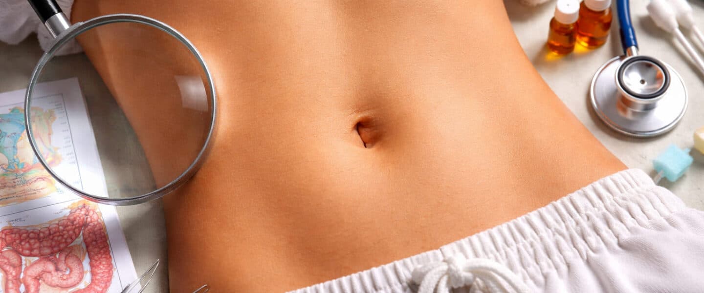 Close-up van een buik met een innie navel, omringd door medische instrumenten zoals een stethoscoop en anatomische tekeningen.
