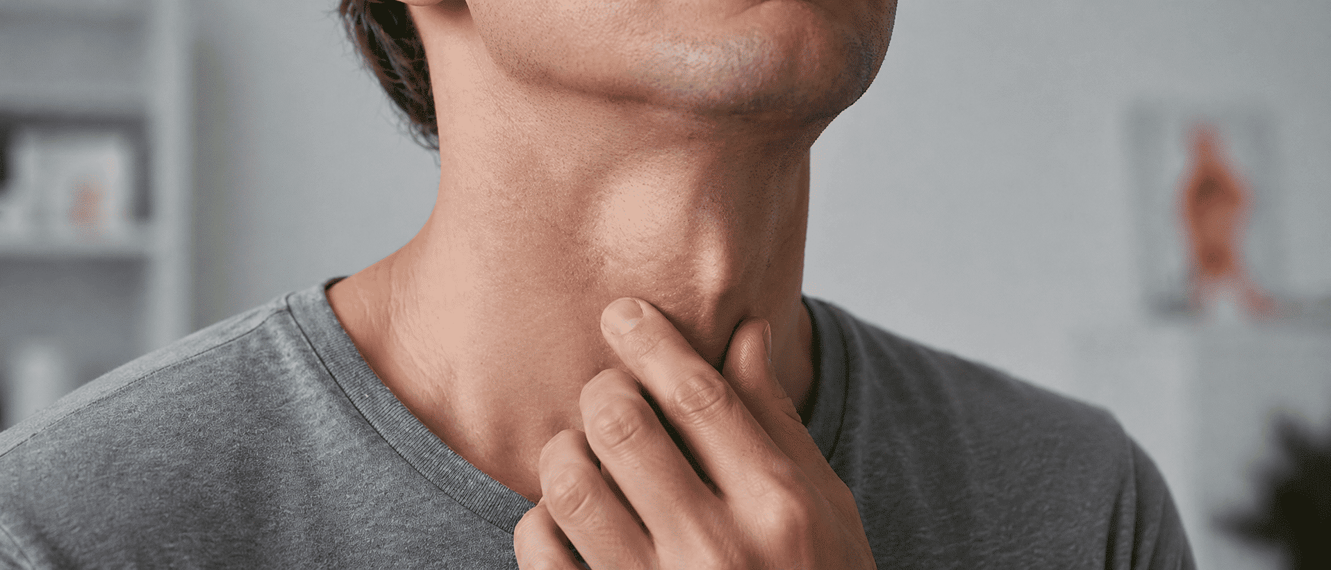 Close-up van een man die met zijn vingers de voorkant van zijn hals bij het strottenhoofd aanraakt, passend bij klachten door clicking larynx syndrome.