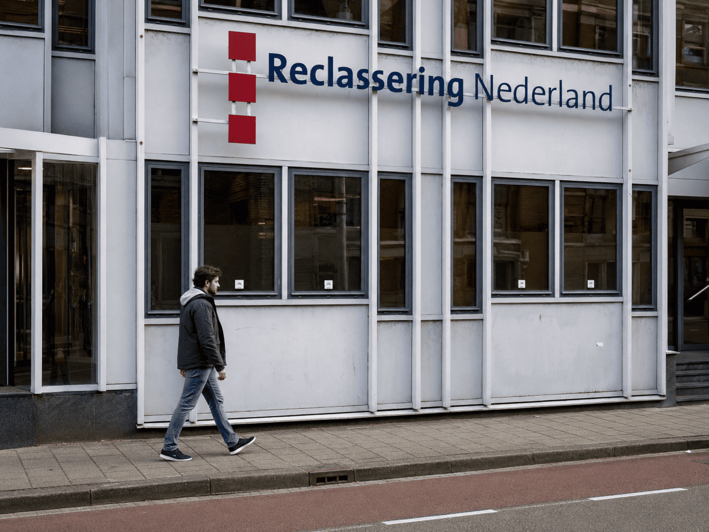 Een man loopt langs het gebouw van Reclassering Nederland, met het logo en de gevel duidelijk zichtbaar op de achtergrond.