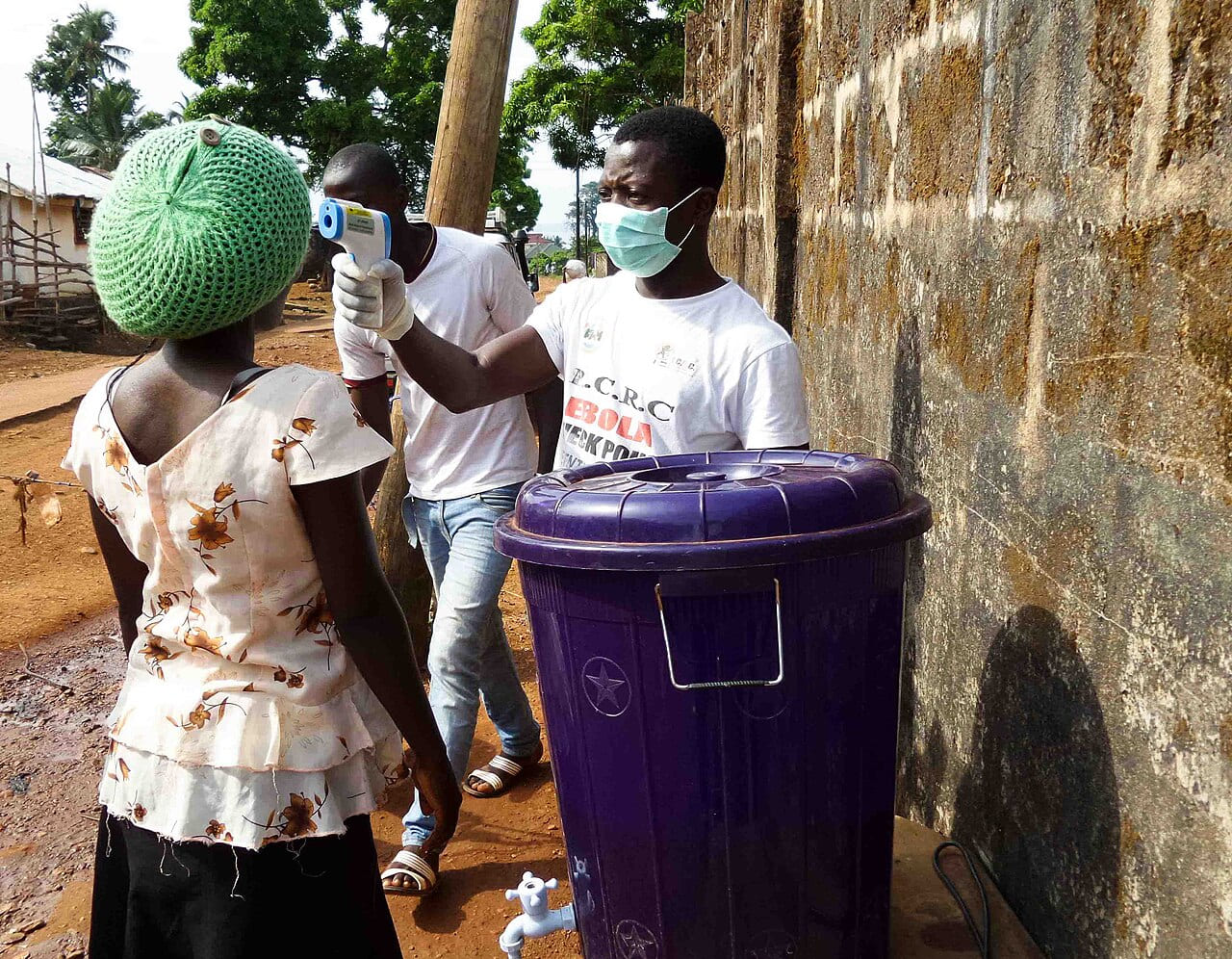 Gezondheidswerker meet bij een vrouw de temperatuur met een infraroodthermometer bij een desinfectiestation tijdens een ebola-uitbraak.