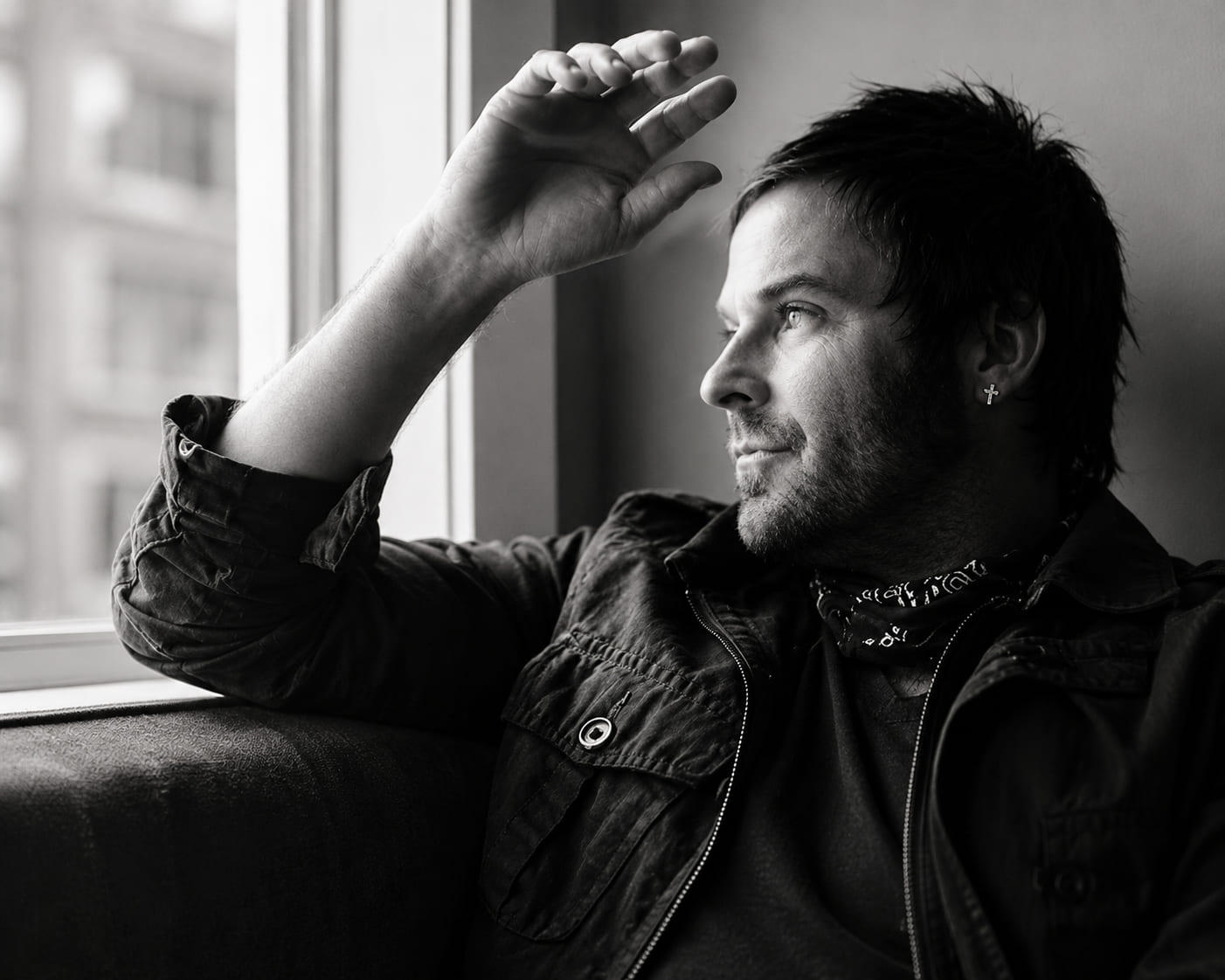 Zwart-witportret van Kevin Max, zanger en voormalig lid van dc Talk, peinzend bij een raam met invallend licht.